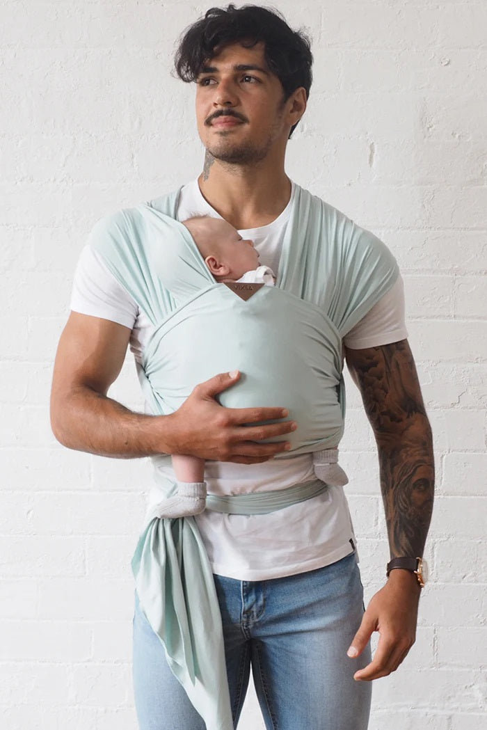 Front view of a man wearing a sage green stretch wrap with a newborn inside