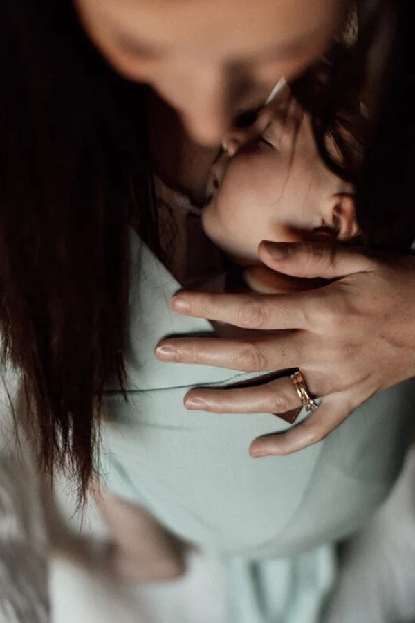 View from above of a baby snuggled into a sage green vixsa stretch wrap on a persons chest