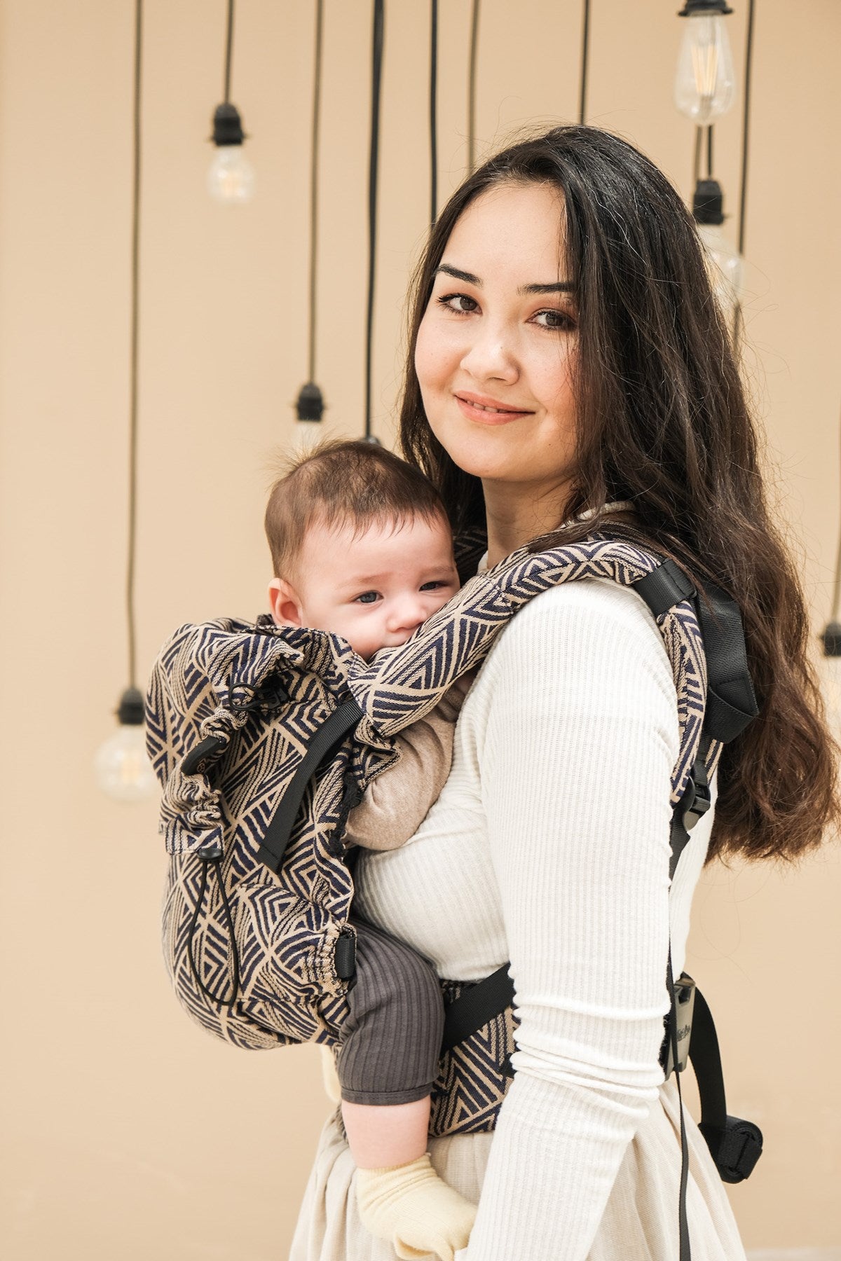 Baby in full buckle baby carrier being worn by a person with long dark hair