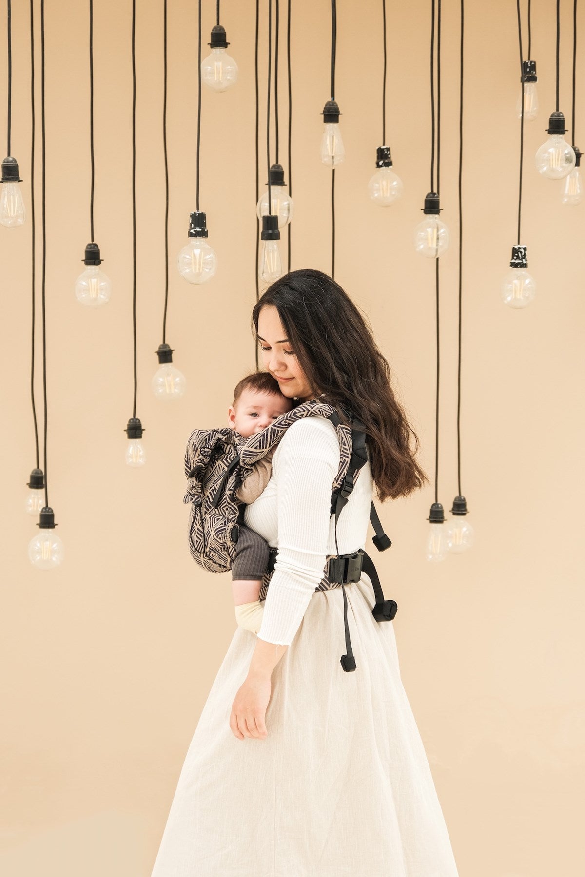 Baby in baby carrier, showing back view of waistband and shoulder straps on a person with long brown hair