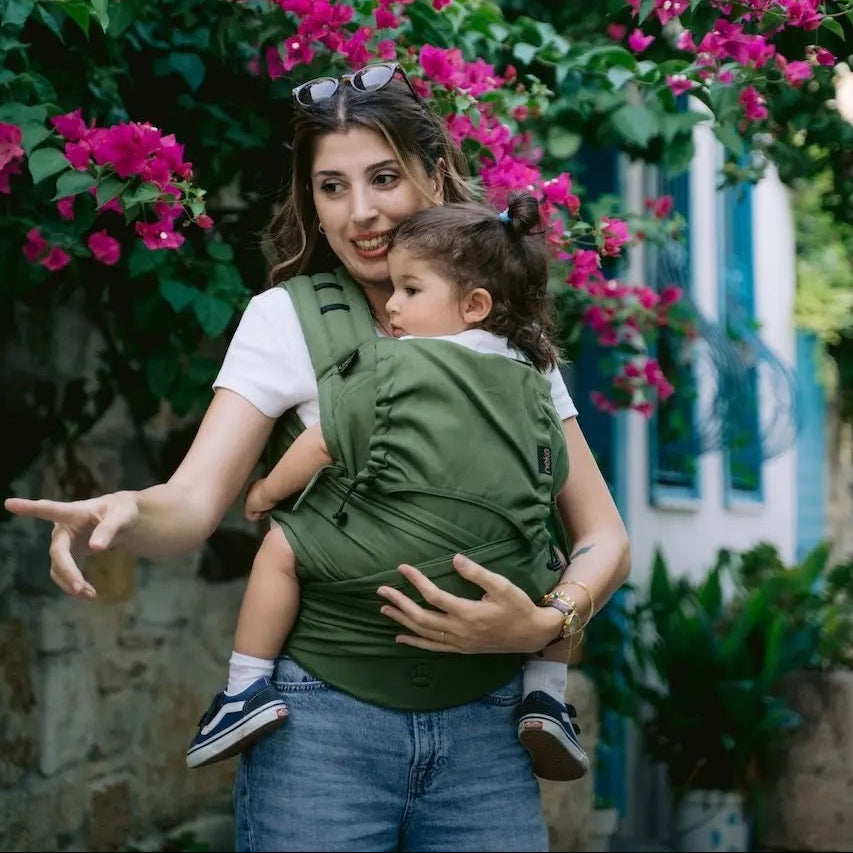 Woman carrying a child in a green baby carrier with pink flowers in the background