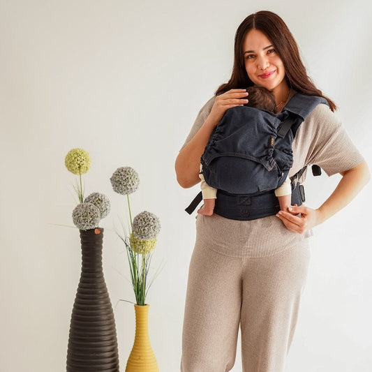 Woman front carrying newborn in denim coloured full buckle carrier