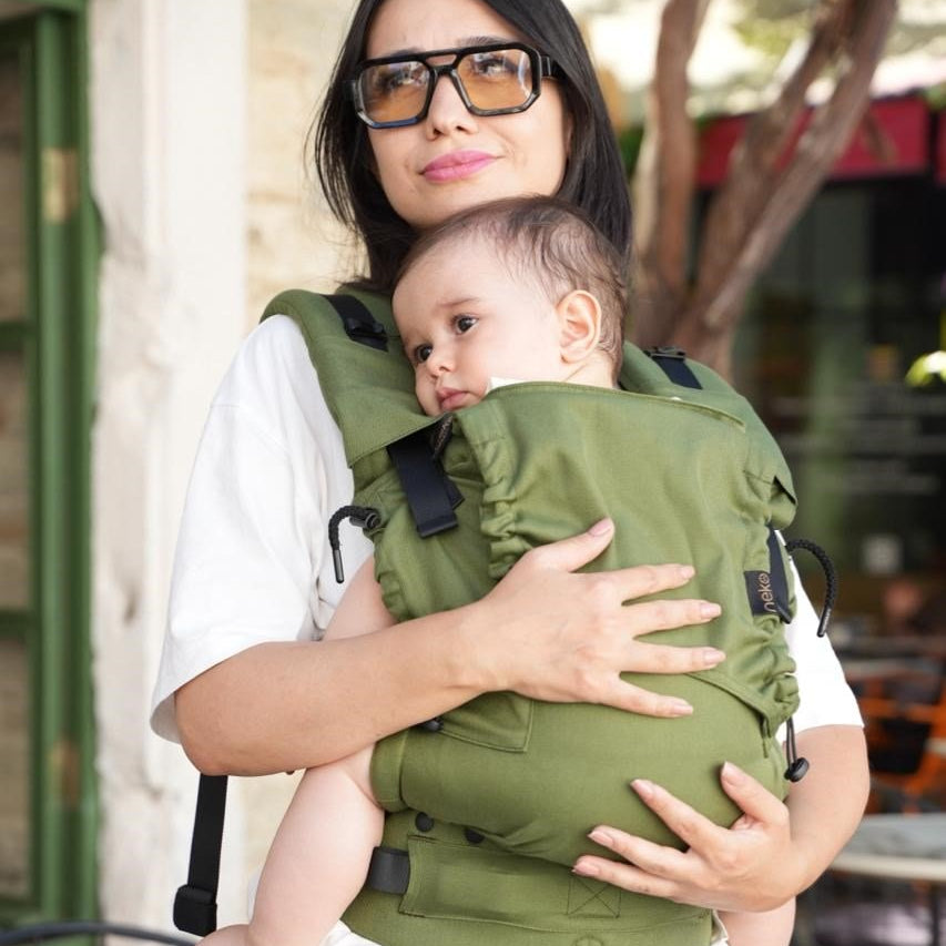 Woman in white clothing carrying baby in green baby carrier