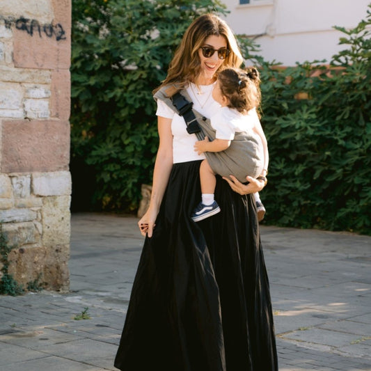 Toddler in grey sling carried by dark haired woman